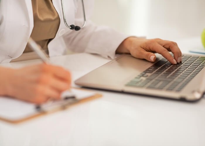 Medical professional sitting at a desk in front of a laptop and a paper chart