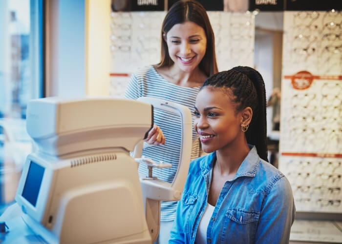 Young woman sitting in front of an optical machine with a technician standing behind her