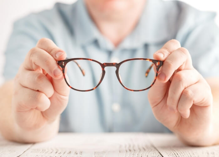 Young man holding a pair of glasses with two hands