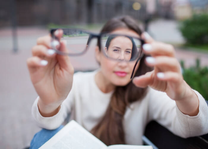 Blurry photo of a woman holding a pair of glasses toward the camera, with only her face seen through the lenses in focus